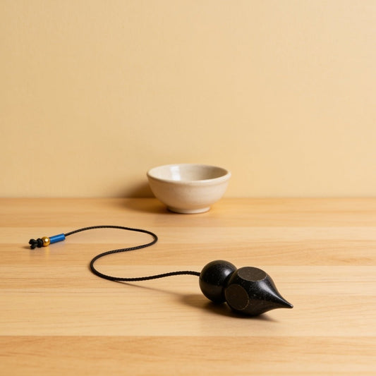 black colour coated brass dowsing pendulum on a plain background