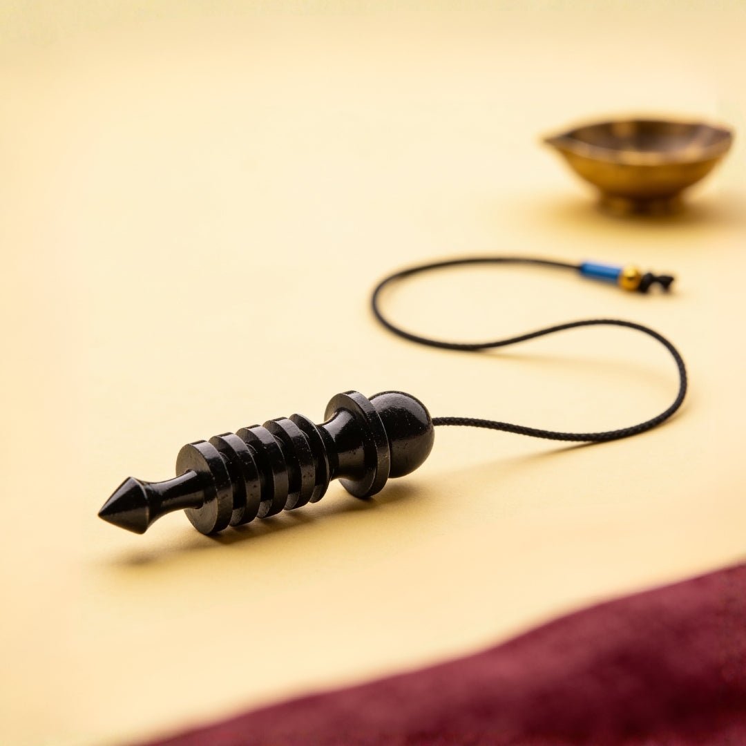 black colour coated brass Isis dowsing pendulum on a plain background